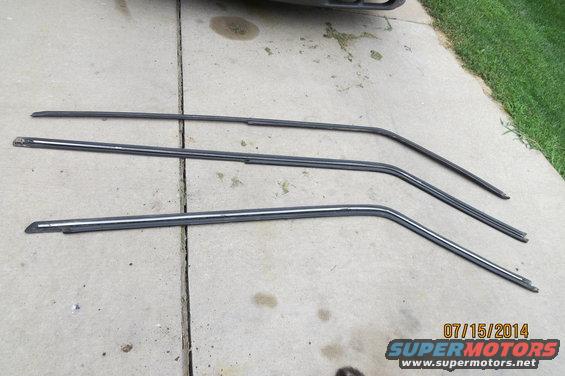 Three dark metal window trim pieces with chrome accents laid on concrete