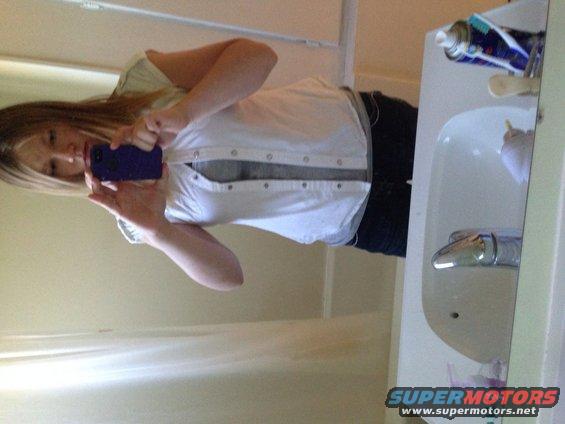 Person holding a purple phone takes a mirror selfie in a bathroom, showing a sink and a can of spray