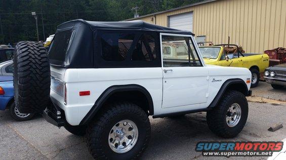 White 1978 Ford Bronco with a black soft top, spare tire on rear, and aftermarket wheels parked outdoors