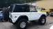 1988 Ford Bronco - A white Ford Bronco with a black soft top is parked next to other vehicles outside a building.