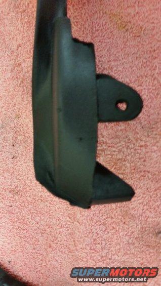 Black plastic automotive part with a mounting tab, resting on a pink textured surface