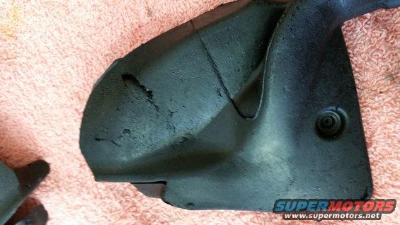 black plastic automotive part with some wear and tear, on a pink fabric surface