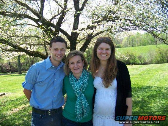 Three people stand in front of a blooming tree in a grassy park