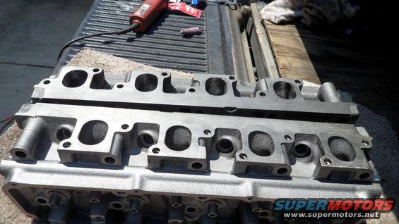 Two engine cylinder heads on a truck bed, with a rotary tool in the background