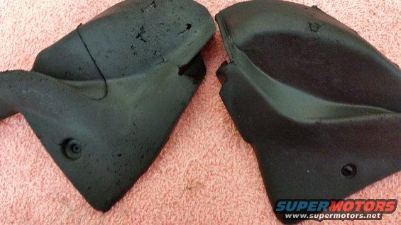 Two black plastic car parts with textured surfaces and visible damage, resting on a pink textured surface