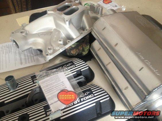 Aluminum intake manifold, two black valve covers with silver stripes and 'POWERED BY FORD' text, and a silver muffler labeled 'Aero Chamber'