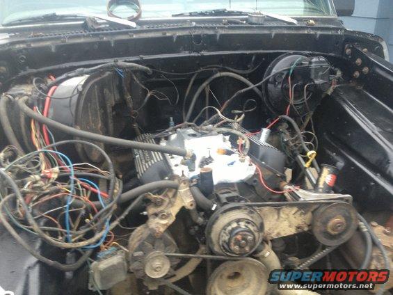 Engine bay with exposed engine components, wiring, and hoses. The engine appears to be a V8 with aftermarket valve covers