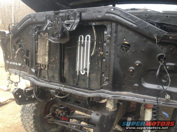 Front end of a vehicle with hood open, showing radiator and engine components. Tires and suspension visible below