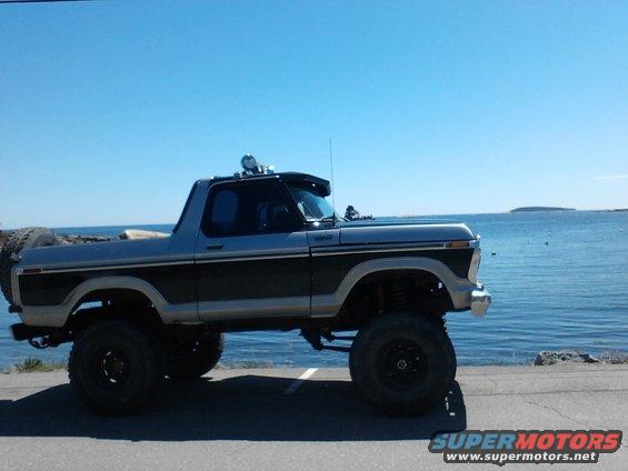Two-tone gray and black lifted Ford Bronco with spare tire on rear, parked by the ocean