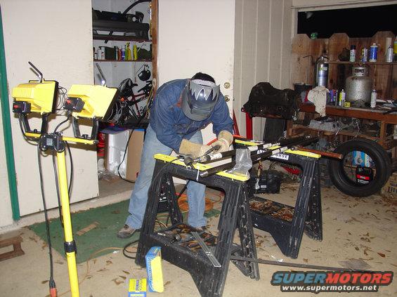 Man in welding mask working on metal frame on sawhorses in garage