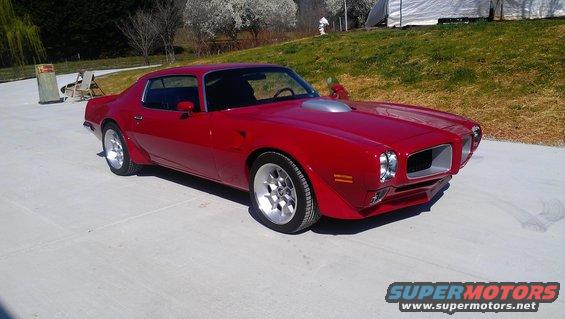 red coupe with hood scoop parked on concrete, trees and grass in background