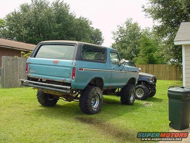 Blue Ford Bronco with lifted suspension and large off-road tires parked on grass next to another dark SUV