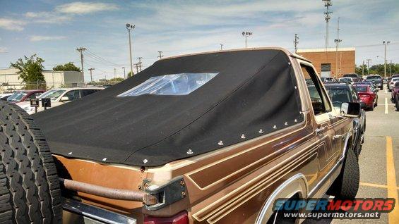 Brown Ford Bronco with a black soft top and a spare tire on the back, parked in a lot
