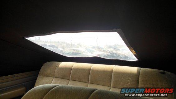 Tan upholstered rear bench seat inside a vehicle with a large, cracked skylight above