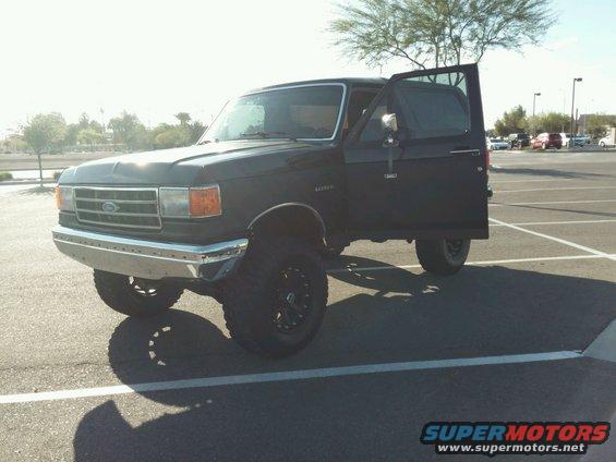 Black Ford Bronco with driver's door open, lifted suspension, and aftermarket wheels parked in a lot