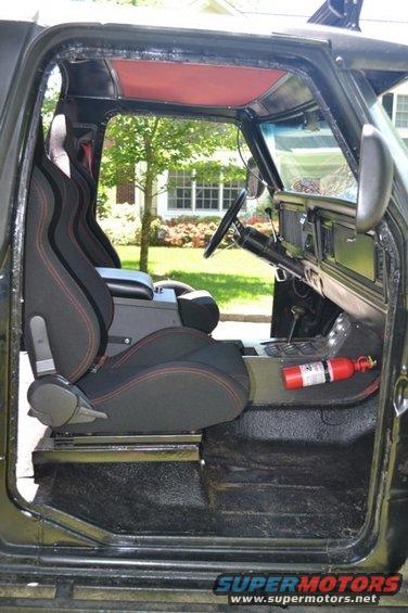 Interior of a dark-colored 1978 Ford Bronco showing racing seats, dashboard, steering wheel, and a fire extinguisher