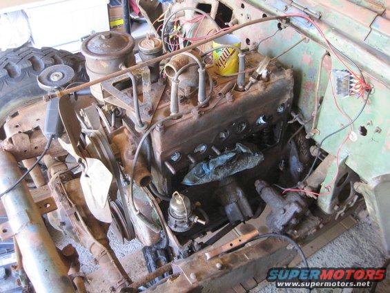 Engine bay with engine block, fan, fuel pump, and wiring visible. Some parts are rusty