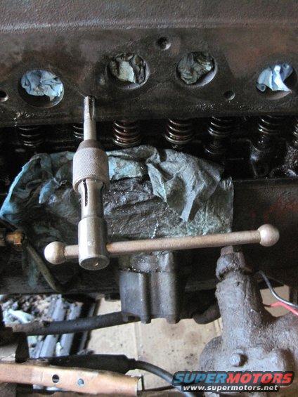 Engine block with valve springs and a valve spring compressor tool. Blue rags are stuffed into cylinder openings