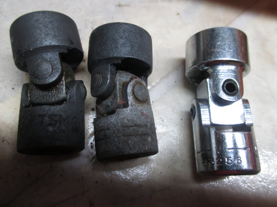 Three universal joints, two old and rusty, one new and shiny. One old one has 'TSM' stamped on it. The new one has '4256' stamped on it