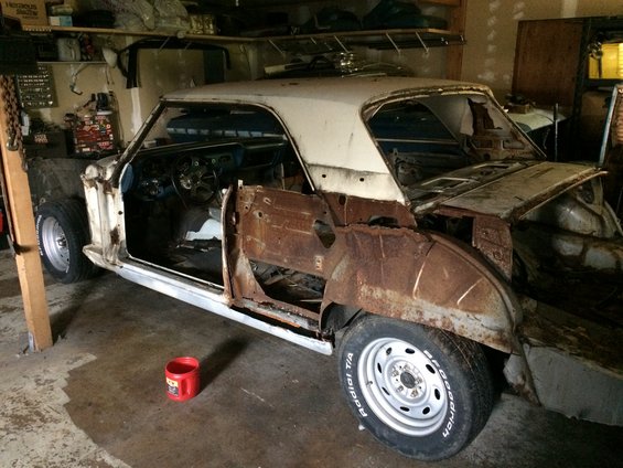 Car body in garage, doors and fenders removed, showing extensive rust damage