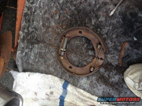 Rusty brake drum assembly with springs and hardware on a dirty surface
