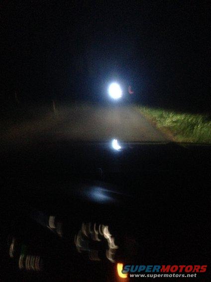 Headlights illuminate a dark road at night, with blurry dashboard lights visible