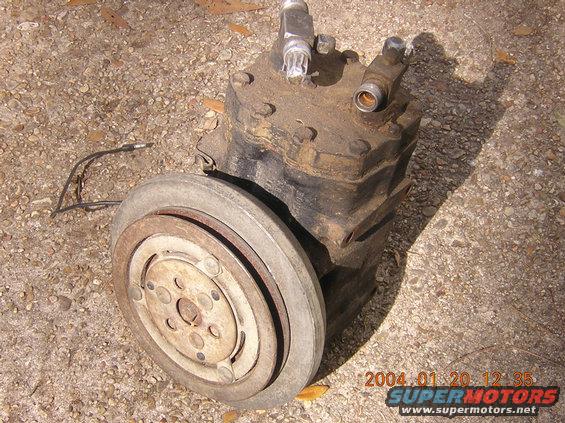Automotive AC compressor with clutch assembly, resting on gravel