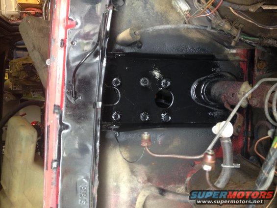 Close-up of a black brake assembly with bolts and brake lines, red painted metal visible