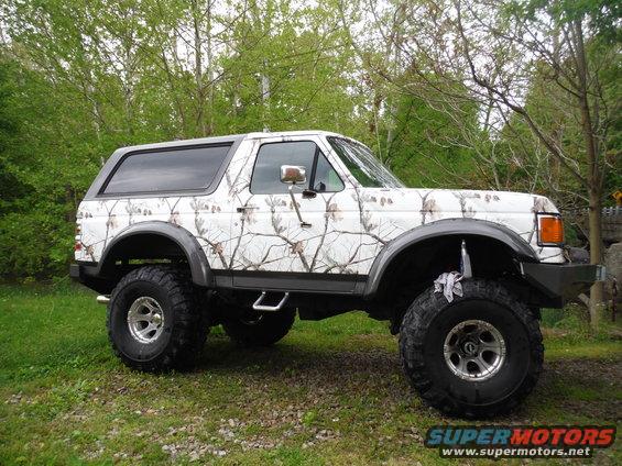 Lifted Ford Bronco with a white camouflage wrap and large off-road tires parked on grass