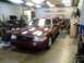 2004 Ford Crown Victoria - A maroon 2004 Ford Crown Victoria is in a garage, possibly being serviced, with a mechanic kneeling near the front bumper.
