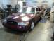 2004 Ford Crown Victoria - A maroon sedan is positioned on a lift inside a garage with tools and equipment visible.