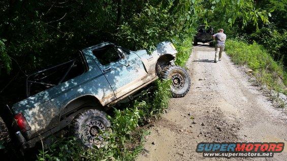 Light blue off-road vehicle with roll cage stuck in mud on a dirt road, front right wheel elevated