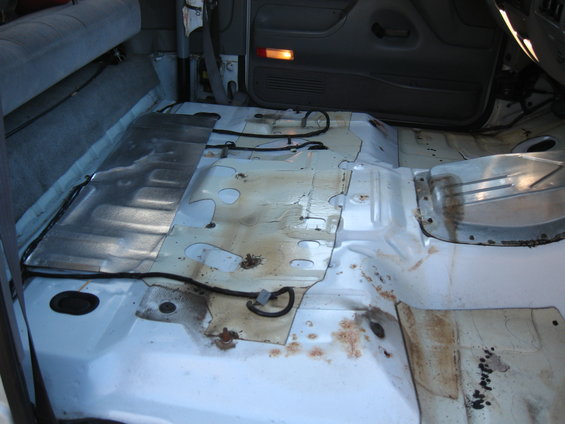 Interior floor panels of a stripped vehicle, showing exposed metal, wiring, and some rust stains