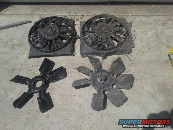 Two radiator fan assemblies and two separate fan blades laid out on a concrete surface