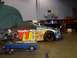 2004 Ford Crown Victoria - A race car with numerous sponsor decals is parked inside a workshop, with a brake rotor on a stand nearby.