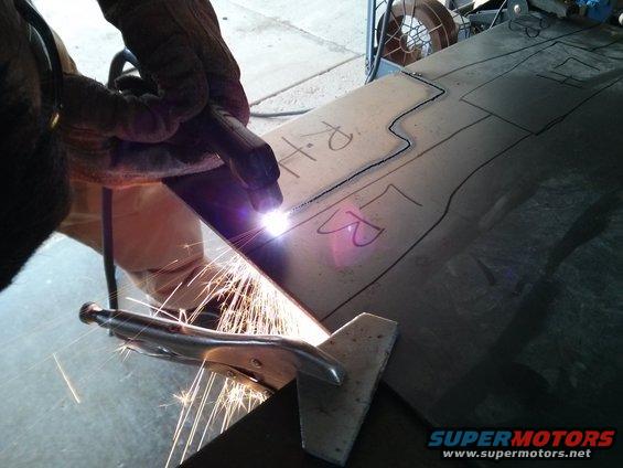 Metal sheet with drawn lines and 'RH' and 'LR' markings being cut by a plasma torch, sparks flying