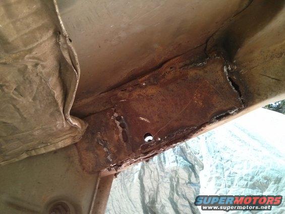 Rusted metal frame with visible welds and a hole, under a tarp