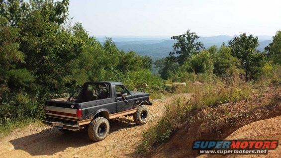 Black 1987 Ford Bronco with a roll cage on a dirt road, rear 3/4 view