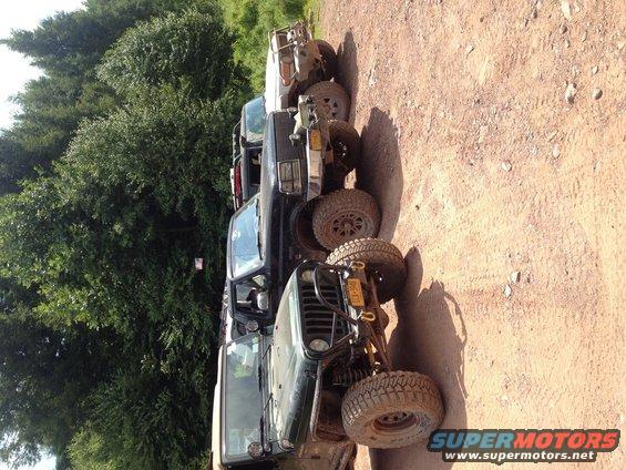 Several off-road vehicles parked in a line on a dirt path, with trees in the background