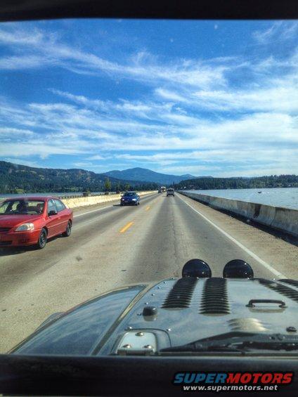 View from inside a Jeep Wrangler, looking out over the hood at a highway with other cars and a body of water to the right