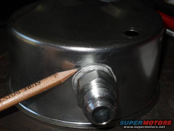 Close-up of a metal gauge with a fitting, a pencil points to a seal