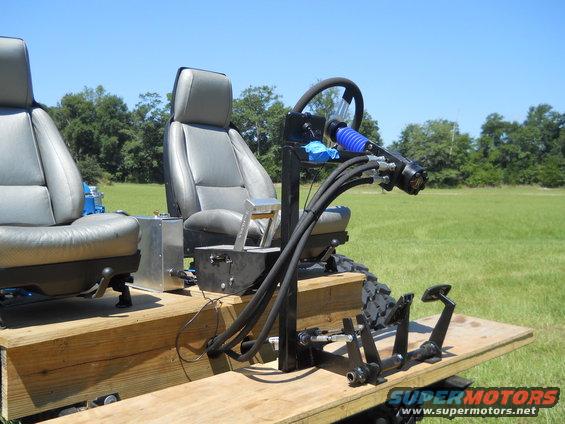 Custom vehicle interior with two gray seats, steering wheel, and control levers on a wooden platform