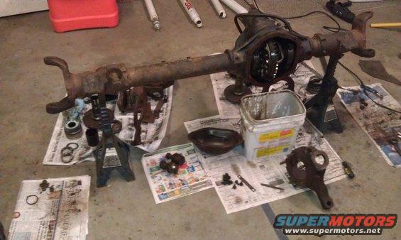 Differential axle assembly disassembled on floor with parts laid out on newspapers