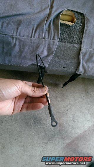 Hand holding a detached seat upholstery cable with a torn seat cushion visible