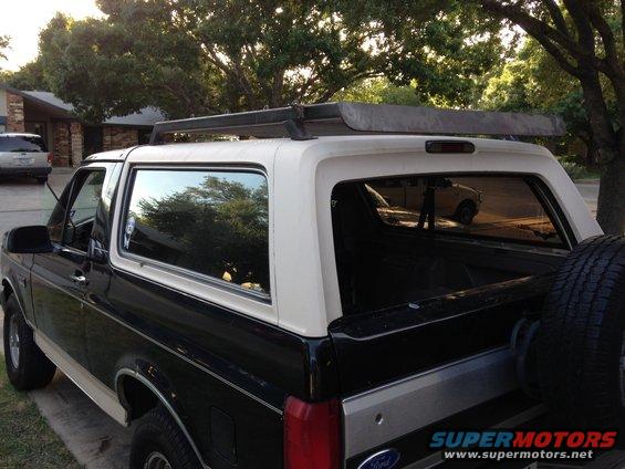 Black and white 1993 Ford Bronco with roof rack, rear-mounted spare tire