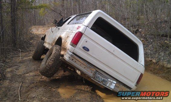 White Ford Bronco tilted on a muddy trail with its tires sunk in