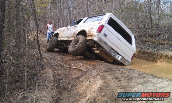 White 1990 Ford Bronco tilted on muddy off-road trail