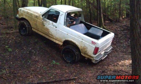 White Ford Bronco II with mud on it driving off-road in a wooded area