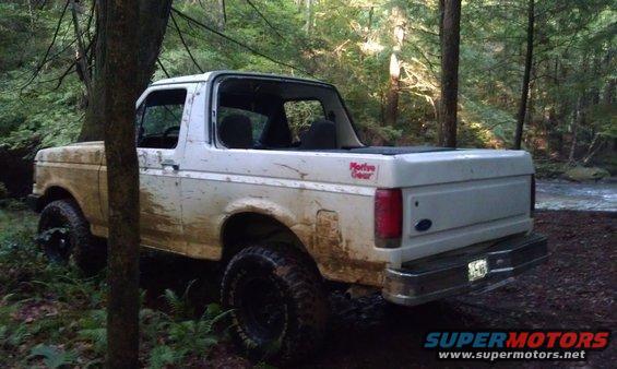 White Ford Bronco parked on a dirt path next to a stream in a forest