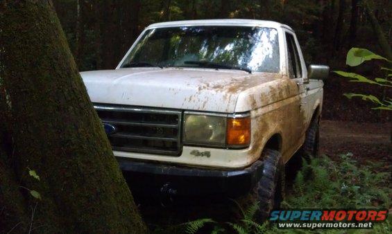 White 1990 Ford Bronco covered in mud, parked off-road